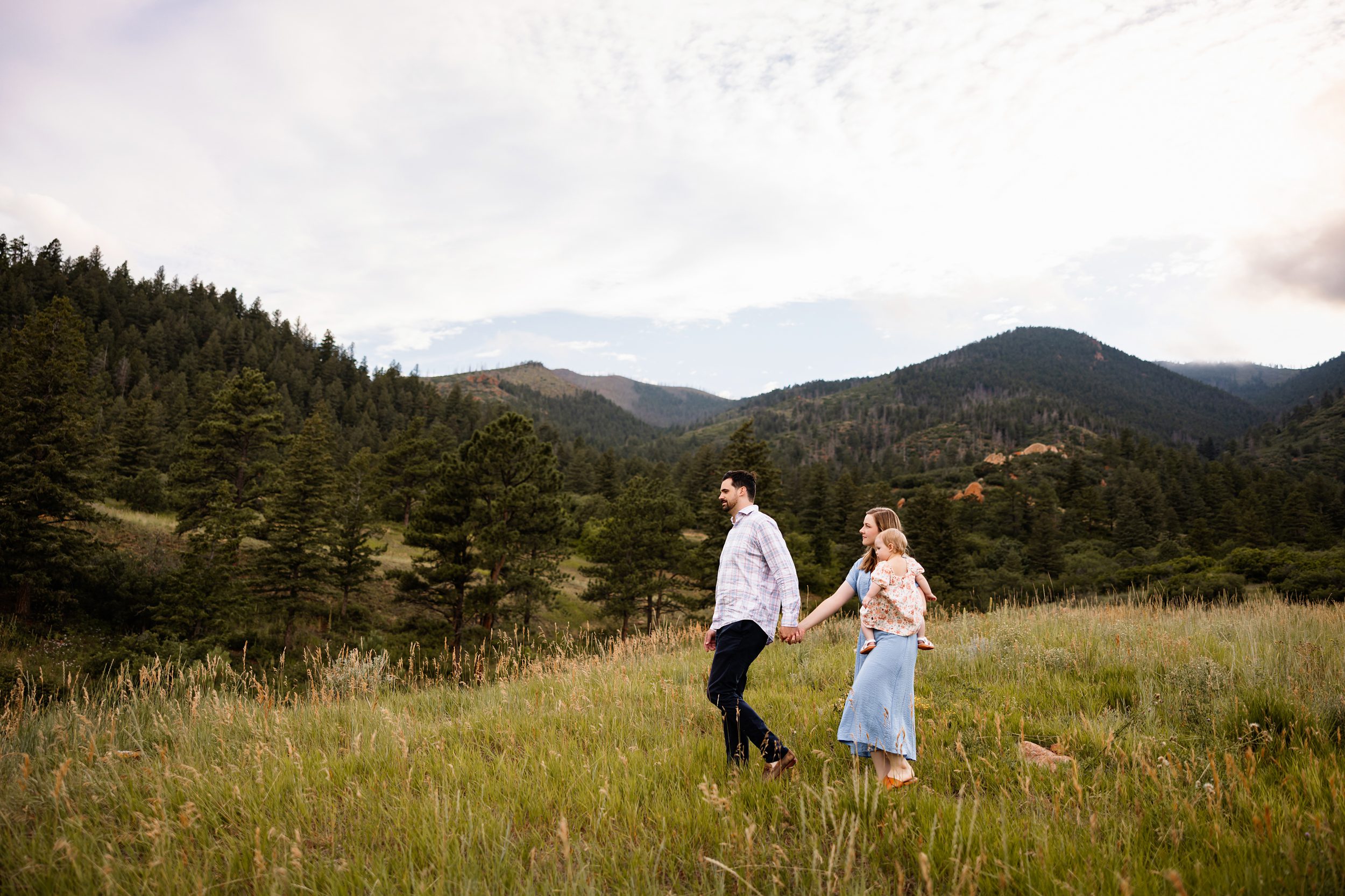 Summer Photo Session in Colorado Springs with a family walking through a lush green field with mountain views