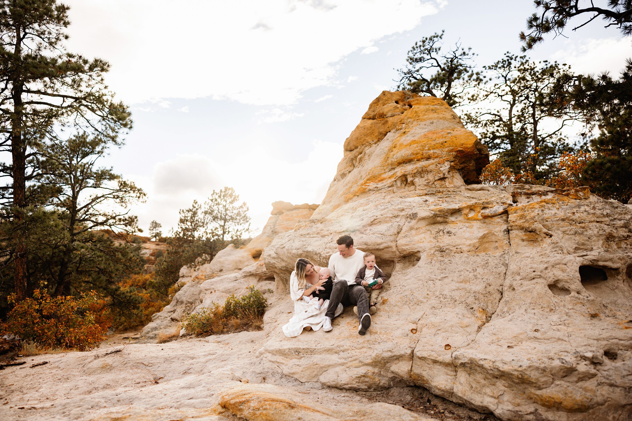 Family sitting on soft sandstone rocks during a golden hour session in Colorado Springs with warm fall tones and natural connection