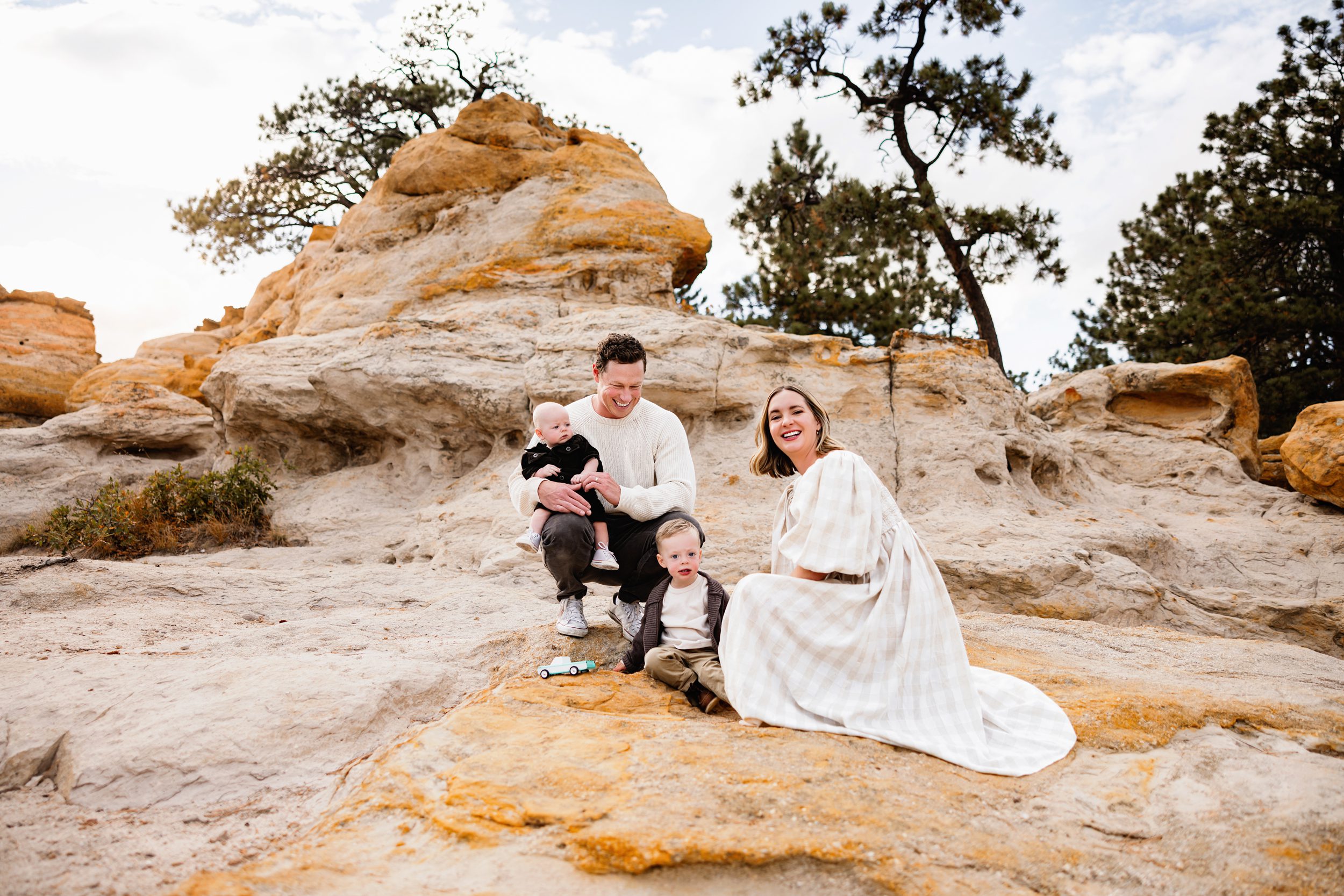 When to schedule your fall photos in Colorado captured with a family sitting together on sunlit rock formations surrounded by soft fall foliage