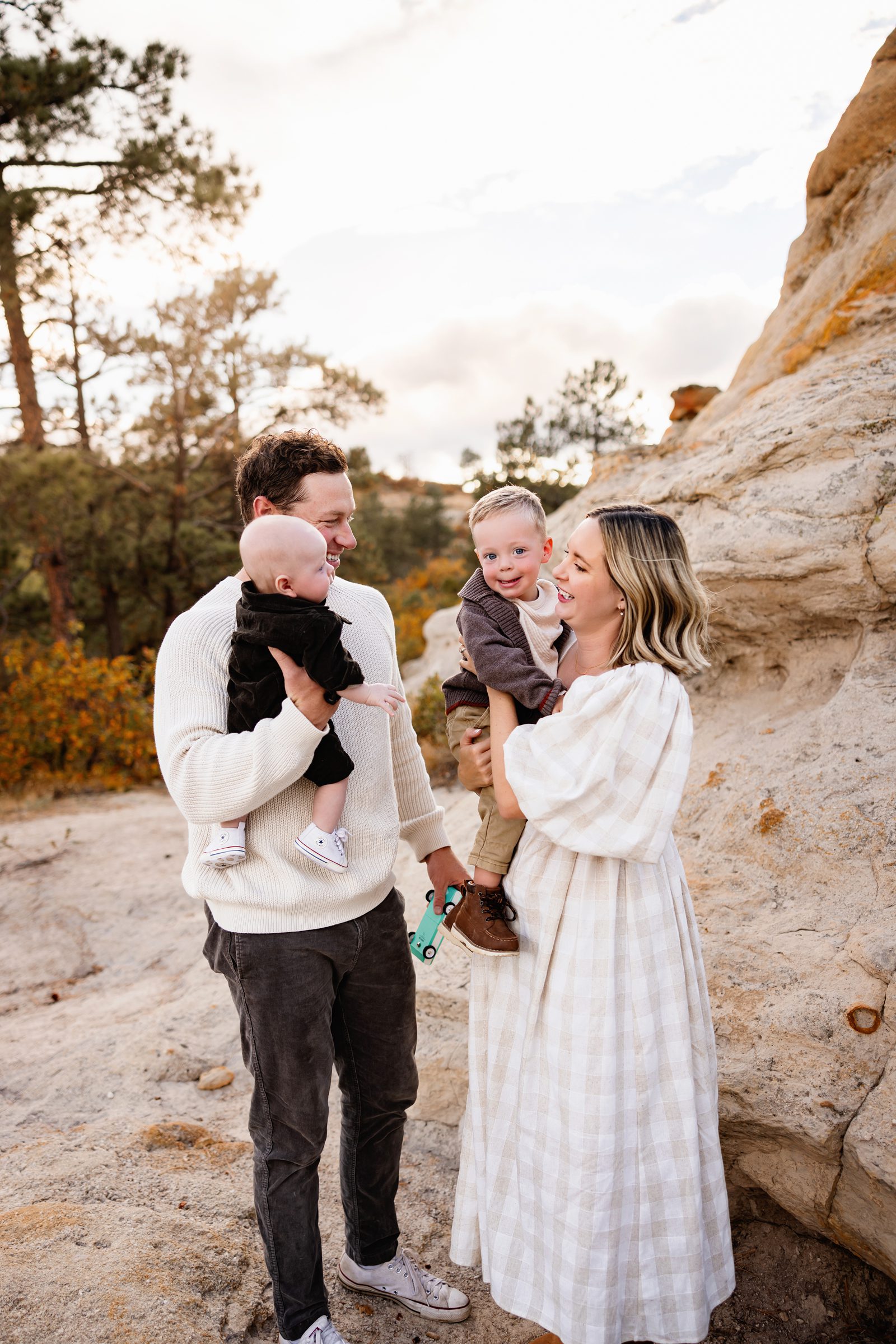 When to schedule your fall photos in Colorado with a smiling family holding their two young children against a rocky natural backdrop at sunset