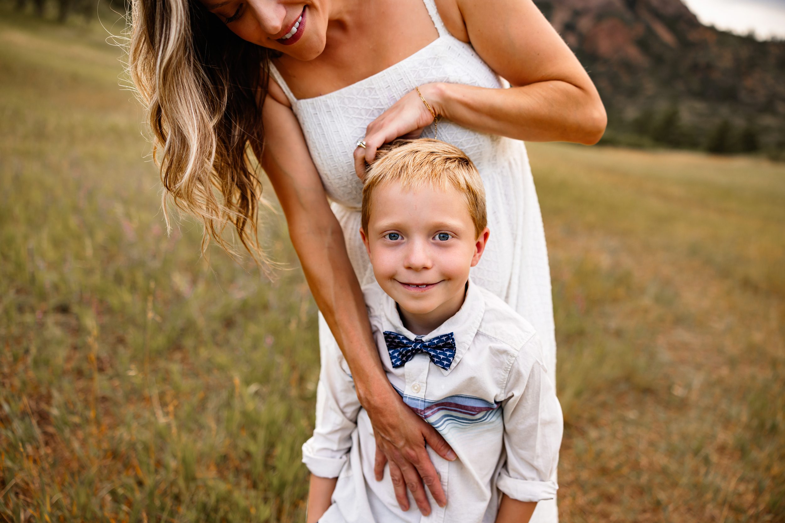 Close-up of a young boy smiling while being hugged by his mom during an outdoor family session