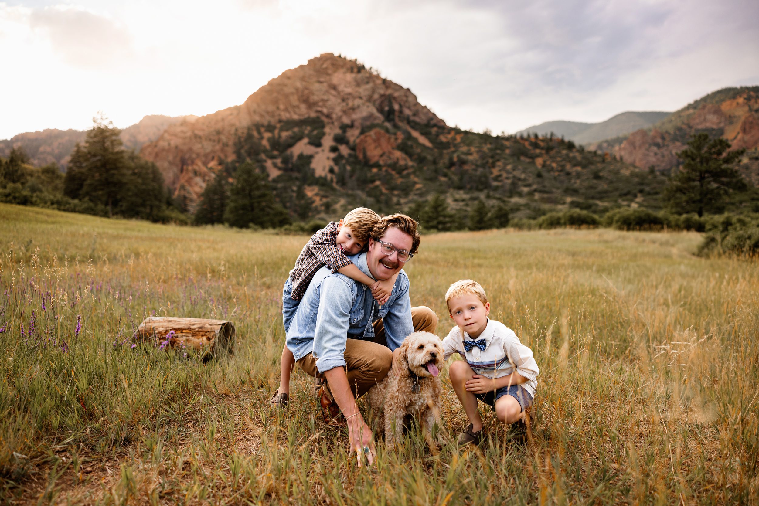 Family photos in North Cheyenne Canon featuring dad and kids sitting in the grass with their dog and mountain backdrop