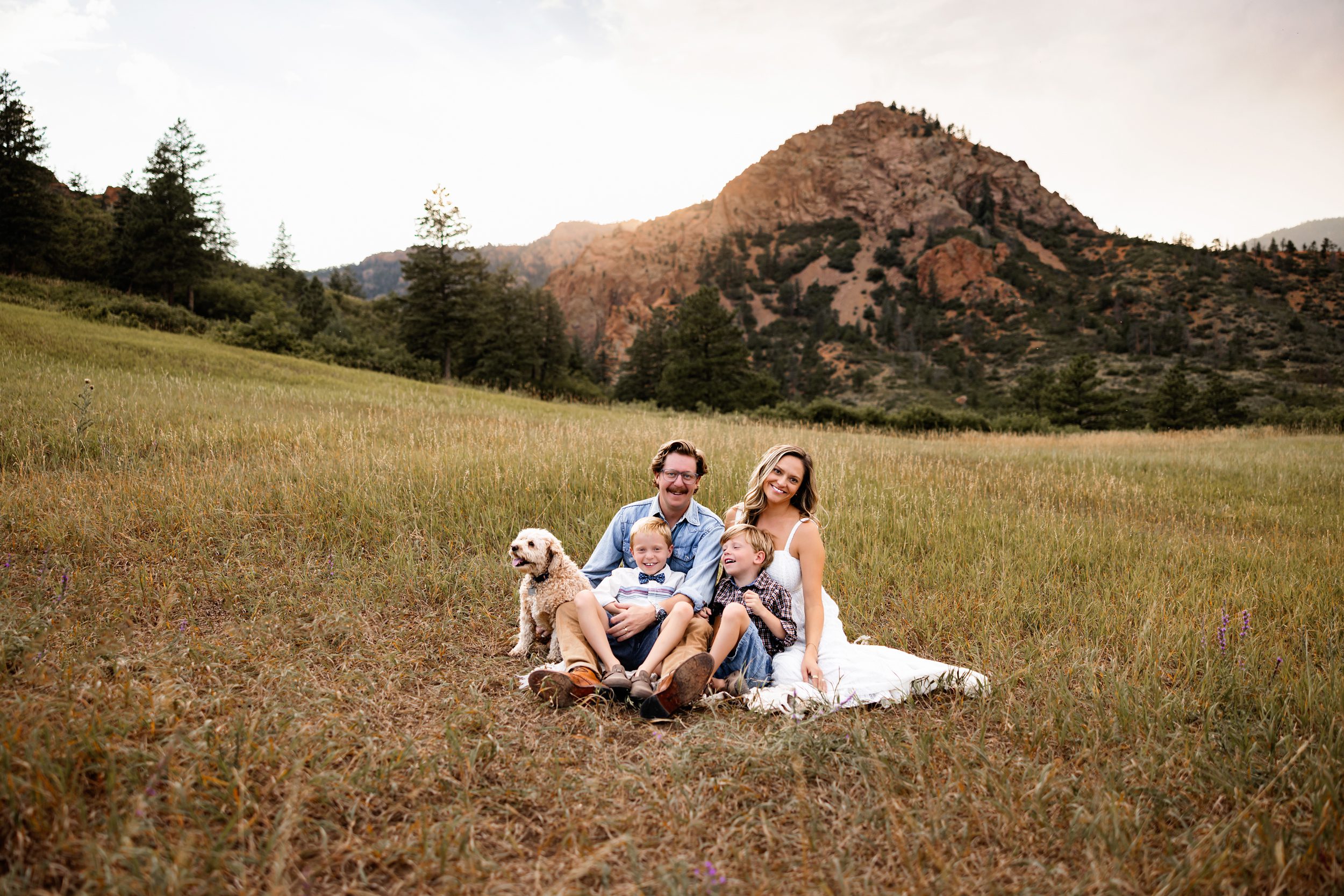 Family sitting together on a blanket in a meadow laughing and cuddling during a sunset session