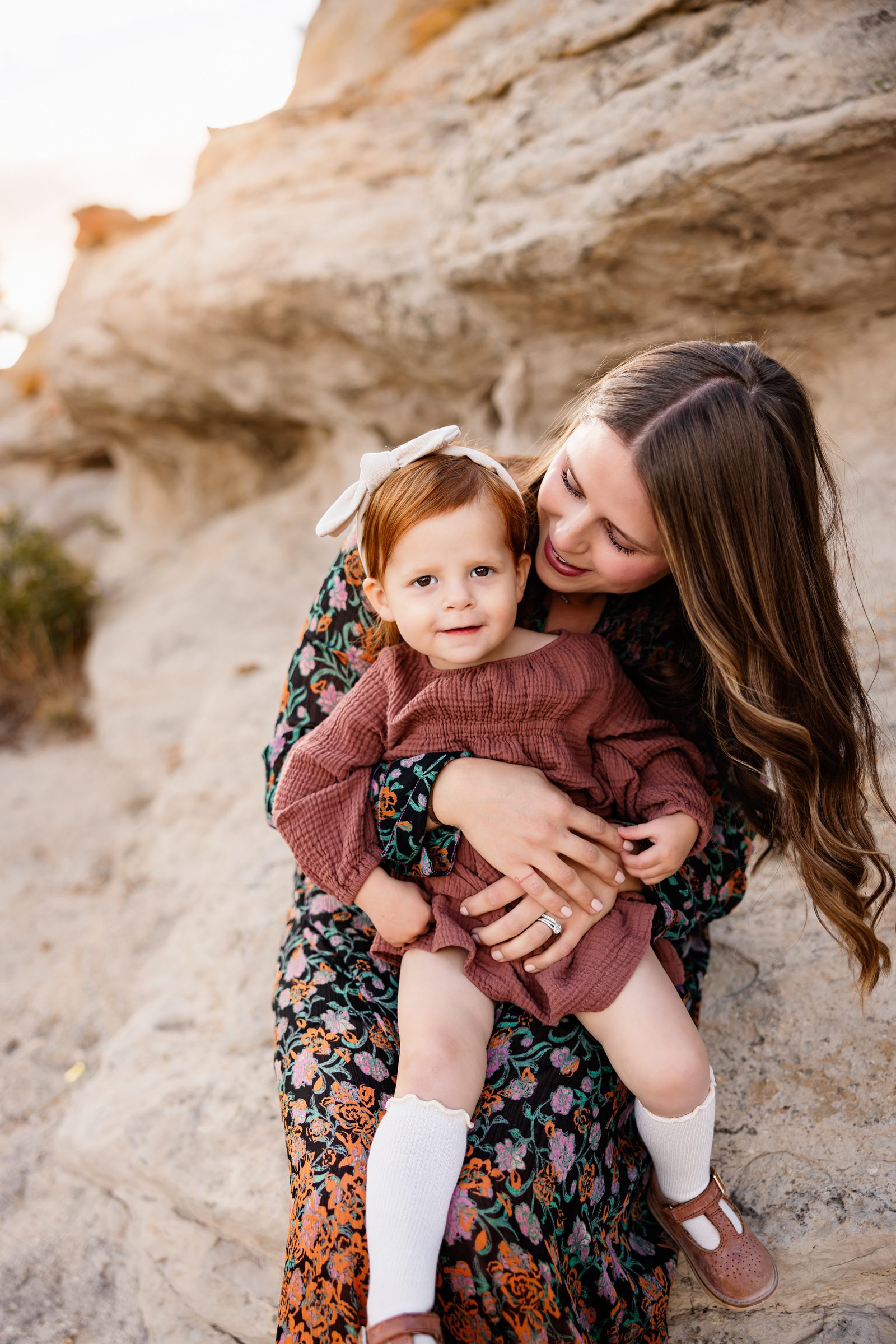 Mom holding her toddler close with soft golden light and neutral rock backdrop