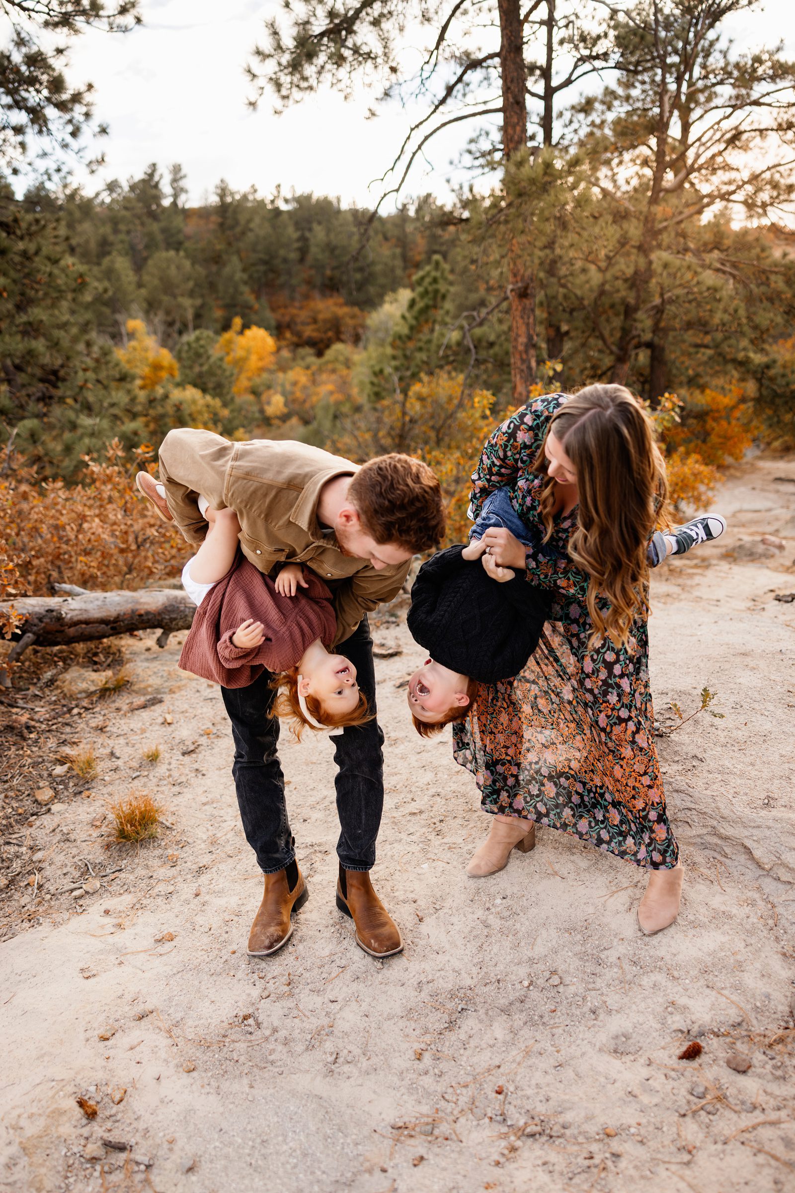 Playful moment of parents holding their toddlers upside down while laughing during an outdoor family session