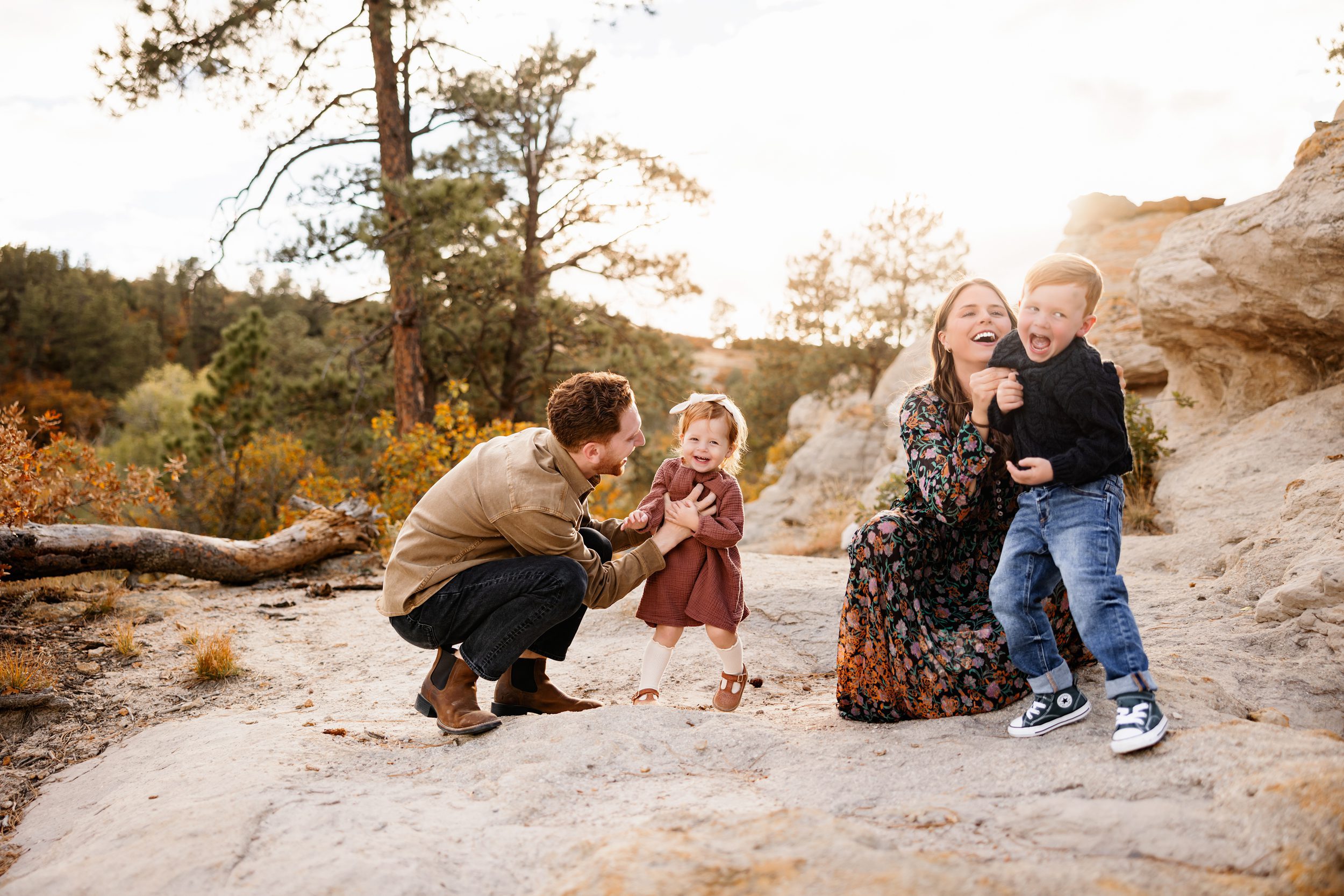 Family sitting together on a dirt path with toddlers smiling and snuggling during an outdoor session