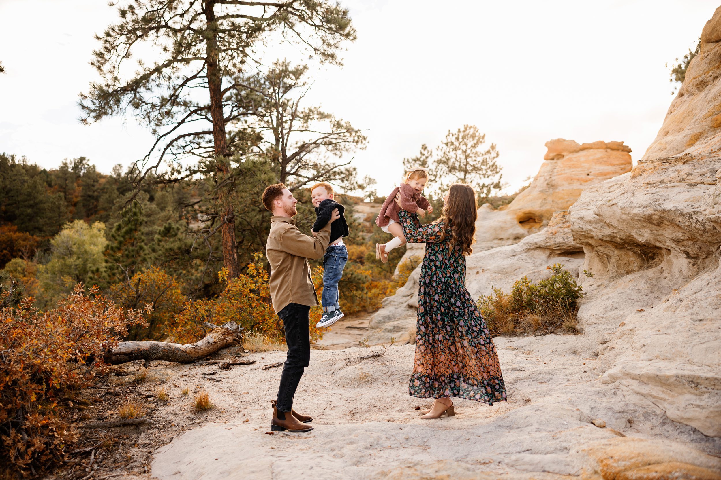 Parents lifting their toddlers into the air during a playful outdoor family session in a rocky landscape