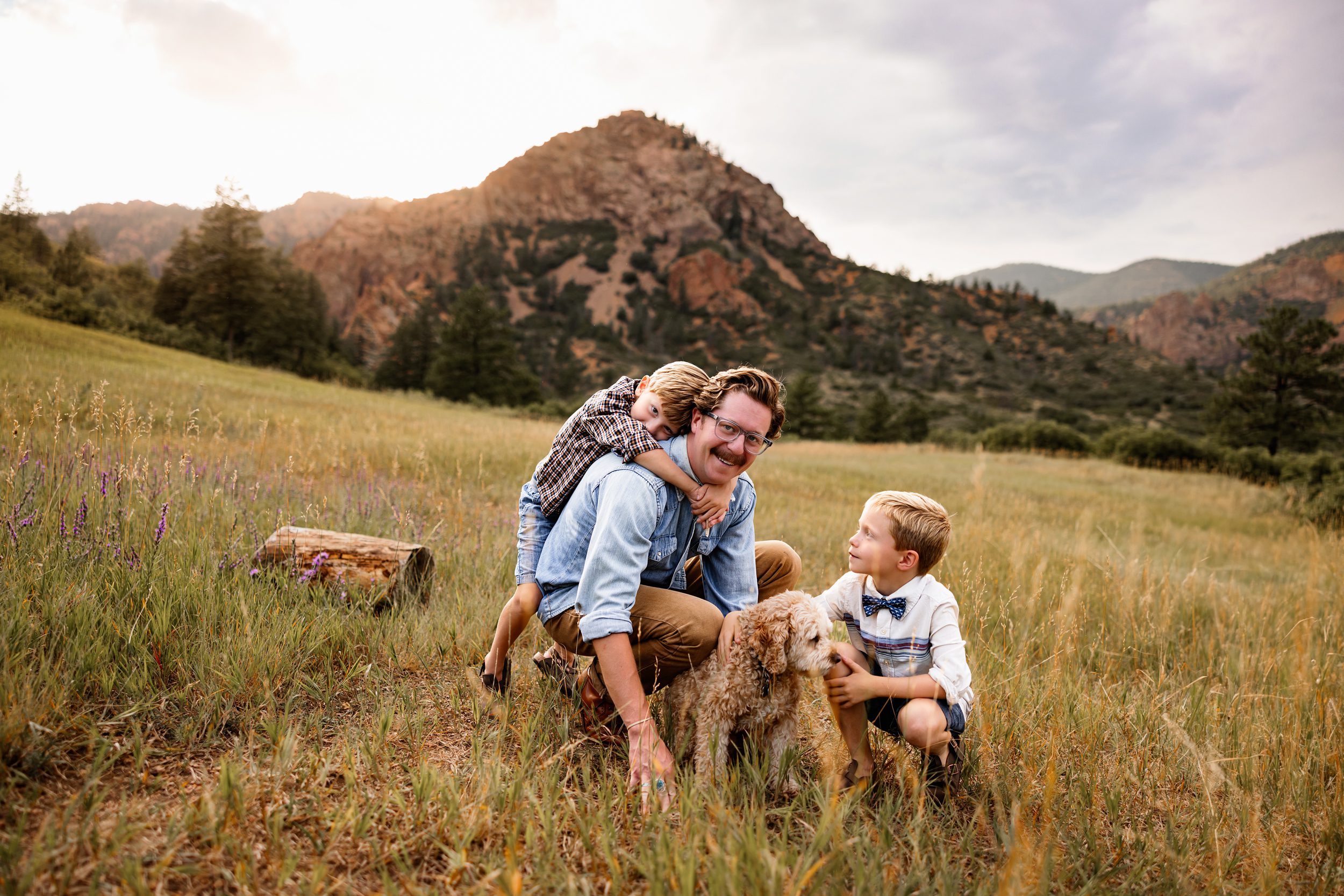 Father with two kids and their dog in a grassy field with mountain views at sunset