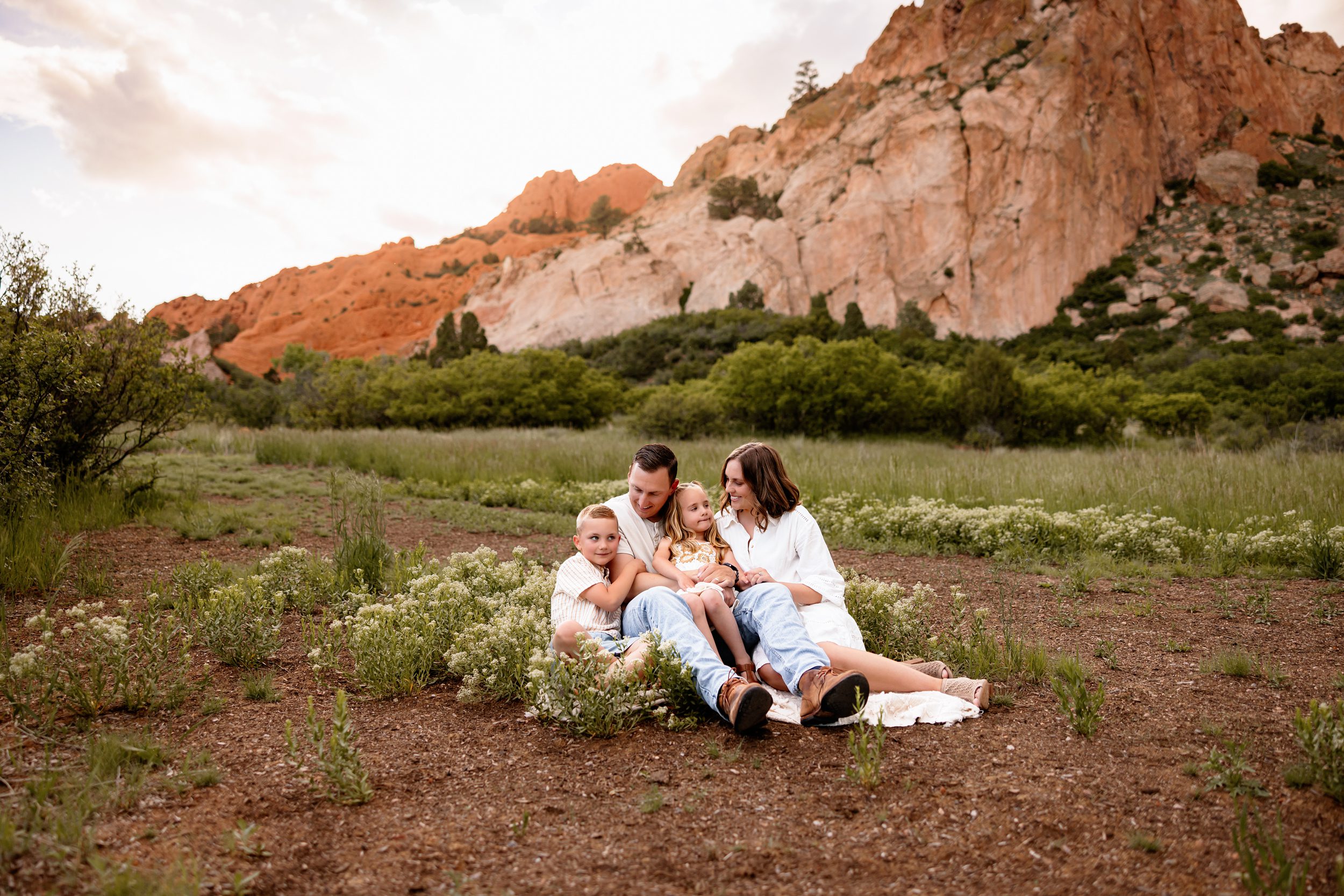 Family sitting together in a grassy field with red rock formations in the background