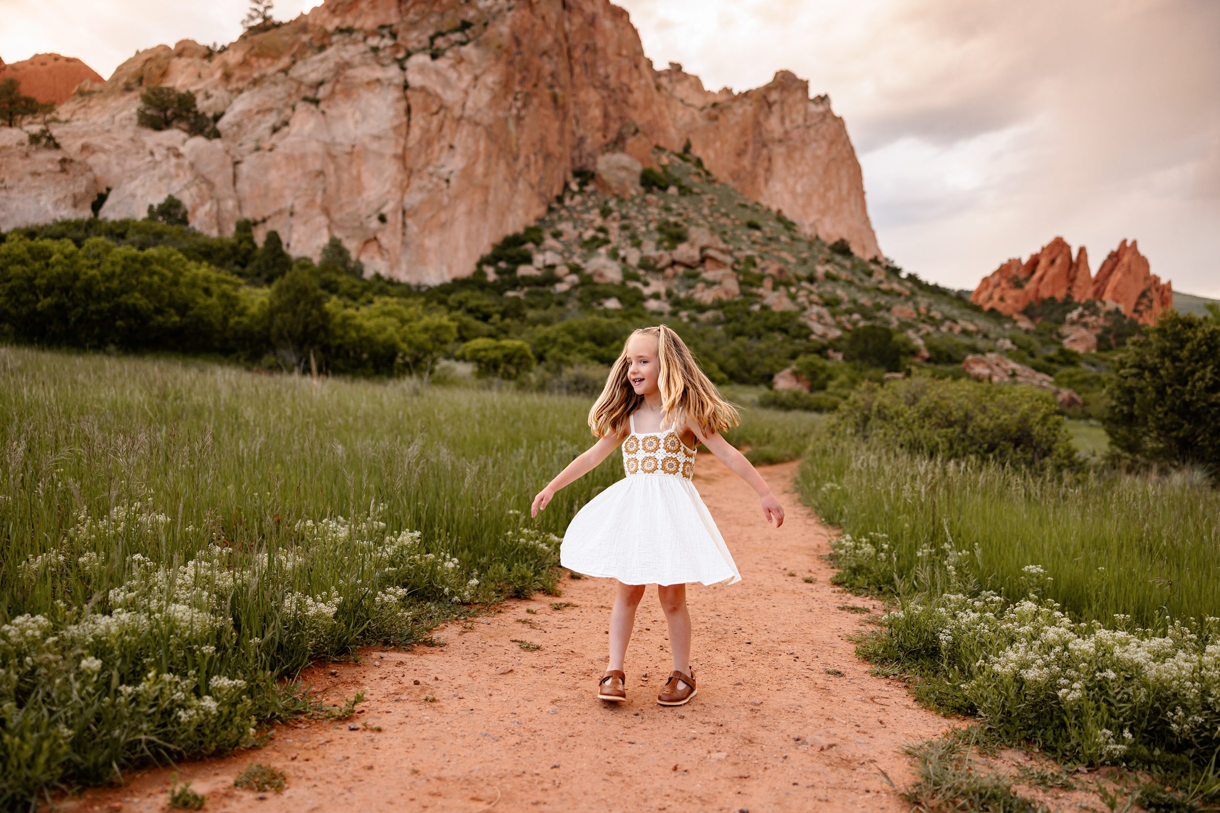 Young girl twirling in a white dress on a trail with red rock views behind her