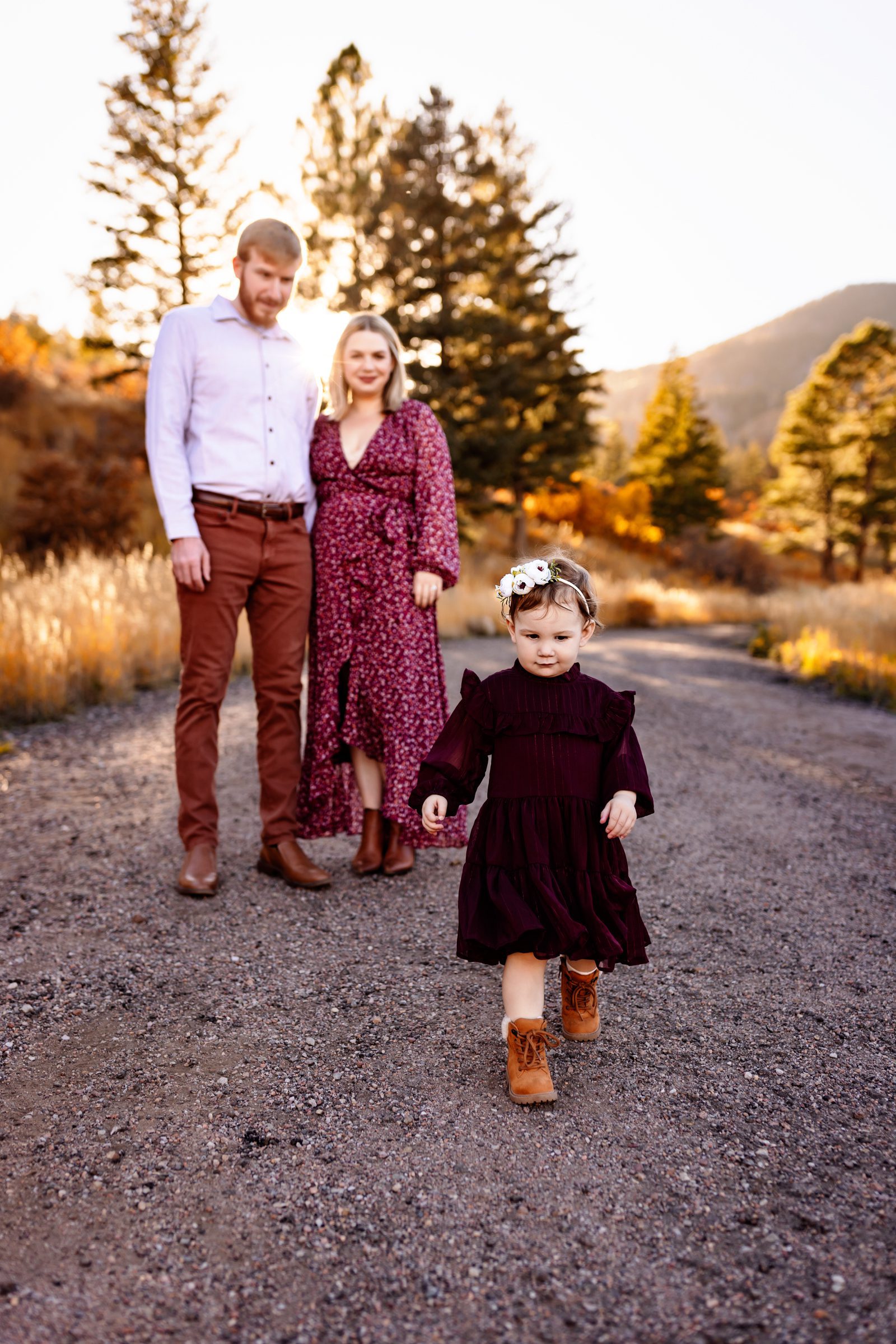 Toddler girl walking confidently ahead of her parents on a gravel road during a fall family session