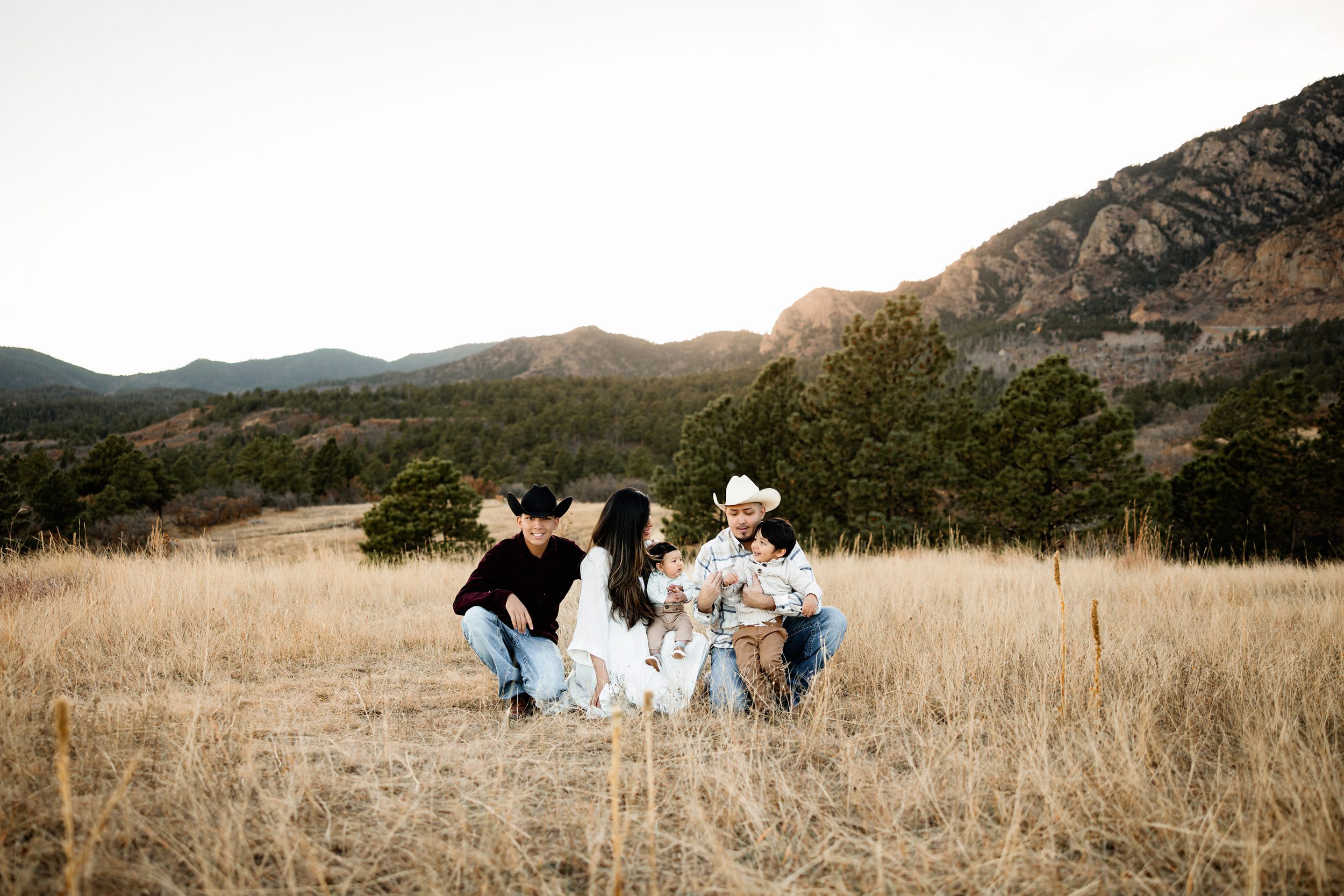 Lifestyle family photos at Cheyenne Mountain with a family sitting together in tall grass, sharing connection and candid moments against a mountain backdrop
