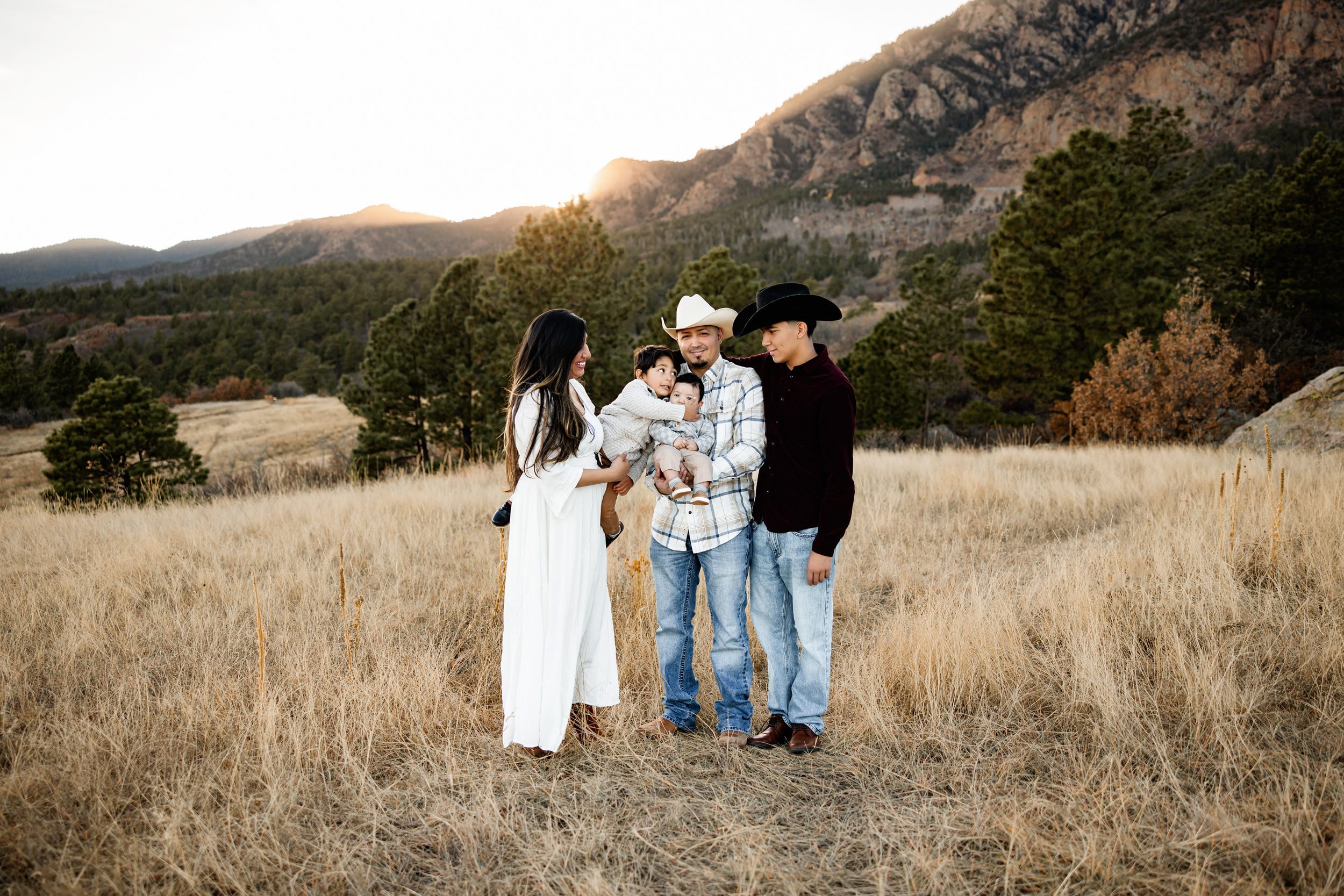 Family photos at Cheyenne Mountain with a family of five standing together in a golden field, mountains glowing in soft sunset light