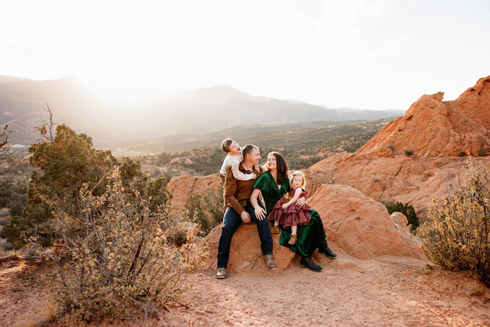 Holiday photos at Garden of the Gods with family sitting on red rocks at sunset, mountain views and warm golden light
