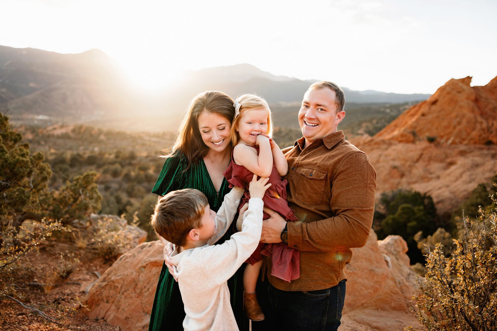 Holiday photos at Garden of the Gods capturing parents holding their children close with glowing sunset light over red rock formations