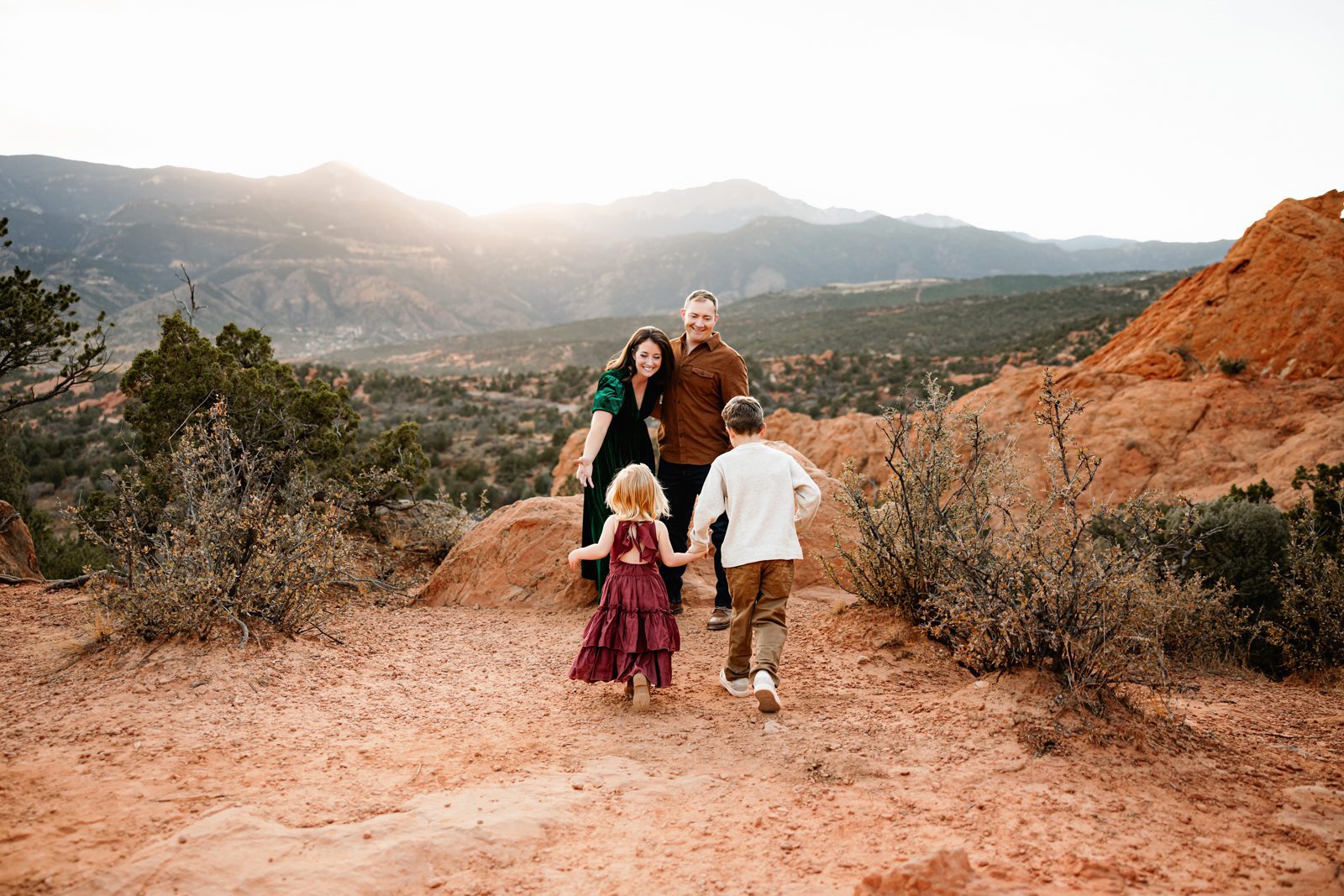 Family exploring red rock formations together with kids running toward parents, warm light and wide mountain backdrop