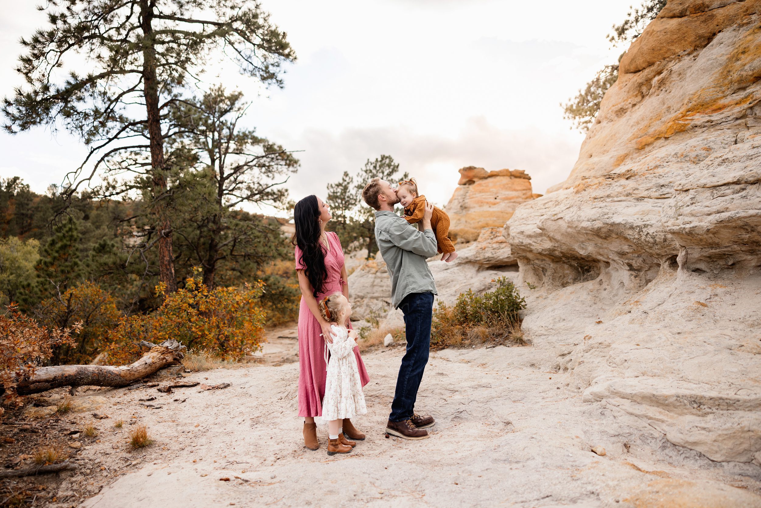 Mini session tips with a dad lifting his baby while mom and toddler watch during a playful outdoor family moment