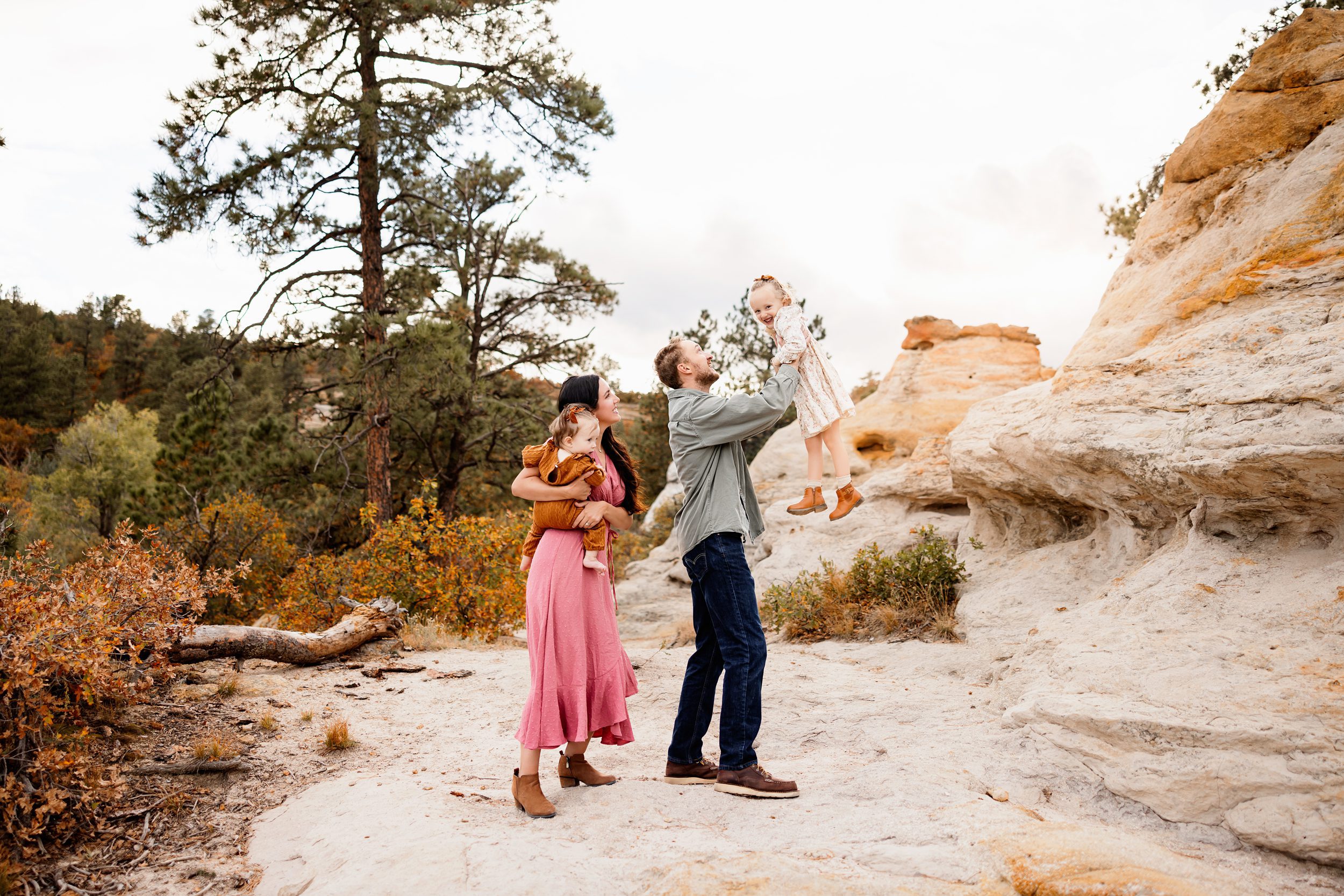 playful moment as a dad lifts his daughter into the air while mom holds the baby nearby