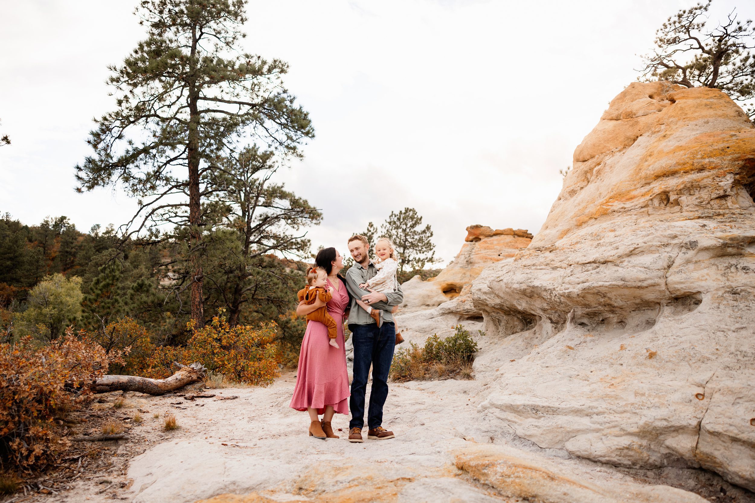 Mini session tips highlighting a relaxed family portrait with parents and two young children standing among trees and rock formations