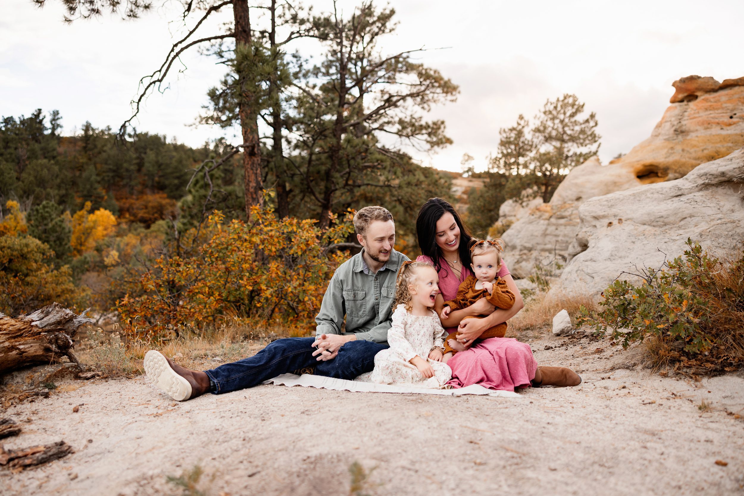 Mini session tips showing parents laughing with their two daughters during a candid seated moment on rocky terrain