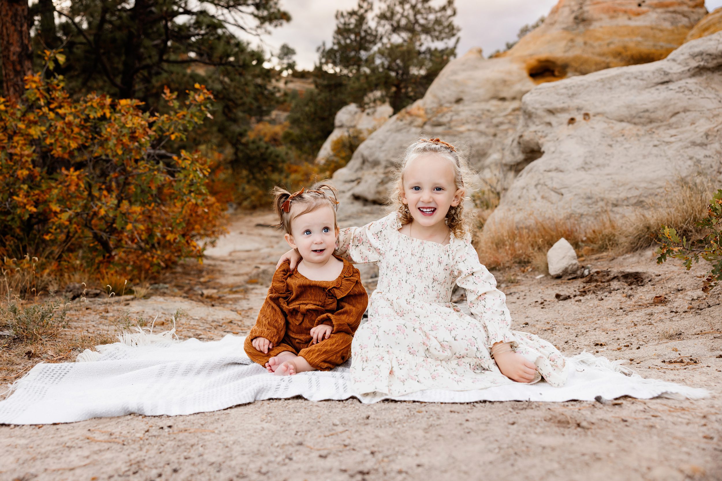two young sisters sitting on a blanket smiling during an outdoor family session