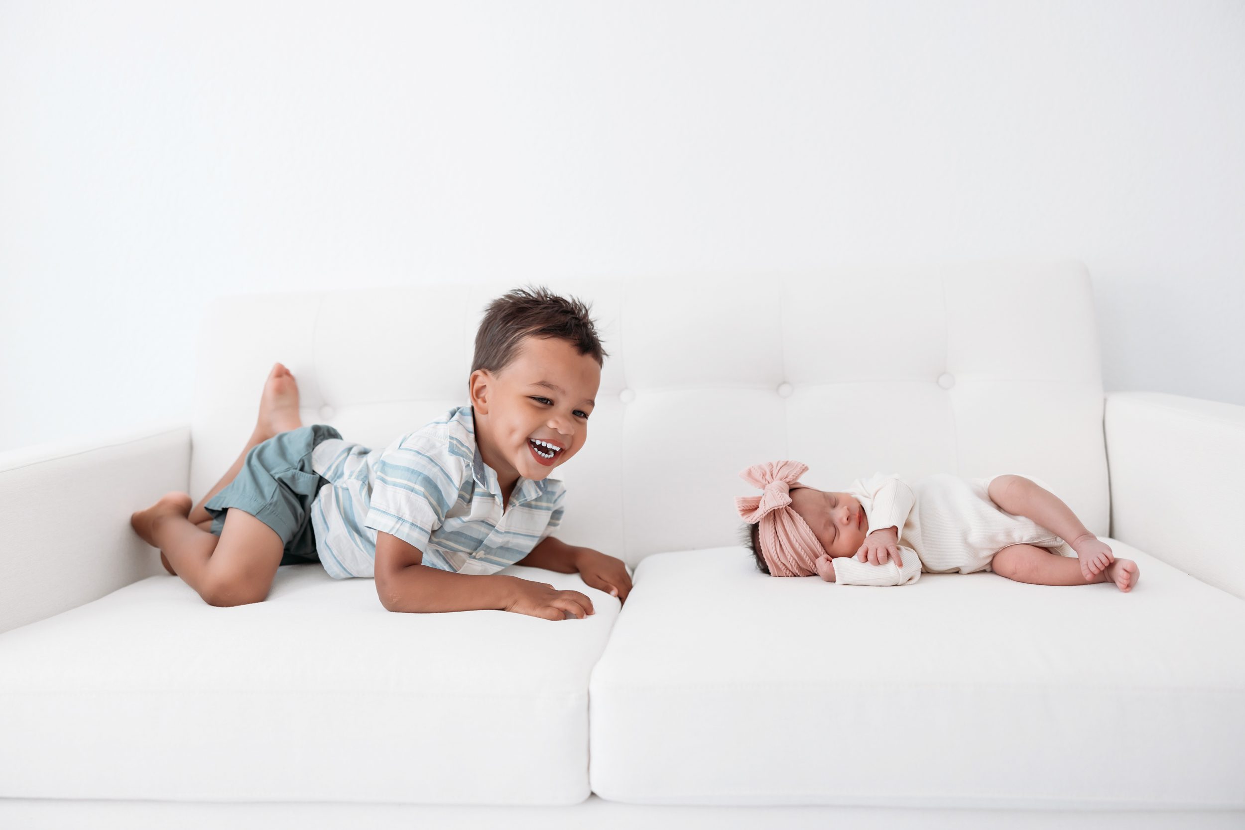 Newborn session in Colorado Springs with toddler smiling on a white couch beside sleeping baby sibling