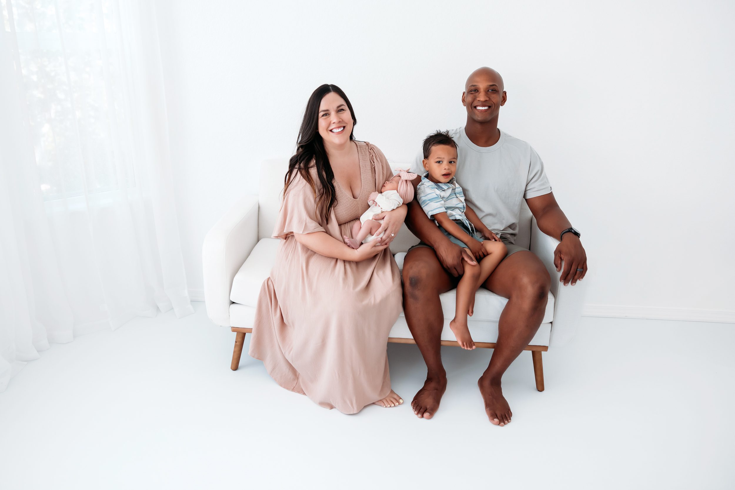 Newborn session in Colorado Springs with parents and toddler interacting gently with their baby on a white couch
