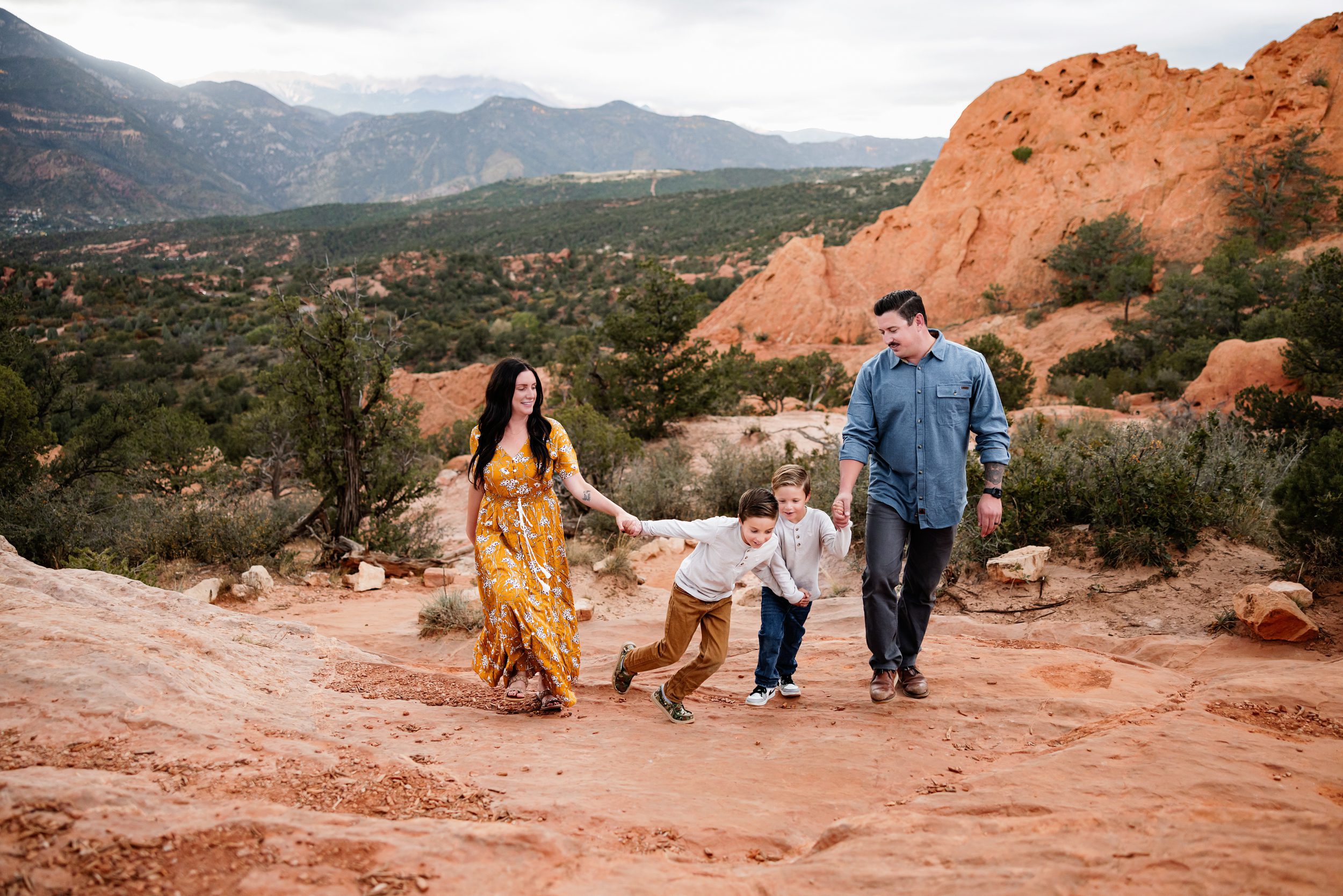 Family walking hand in hand across red rock terrain with mountains in the distance under cloudy skies, showing weather changes on your session day
