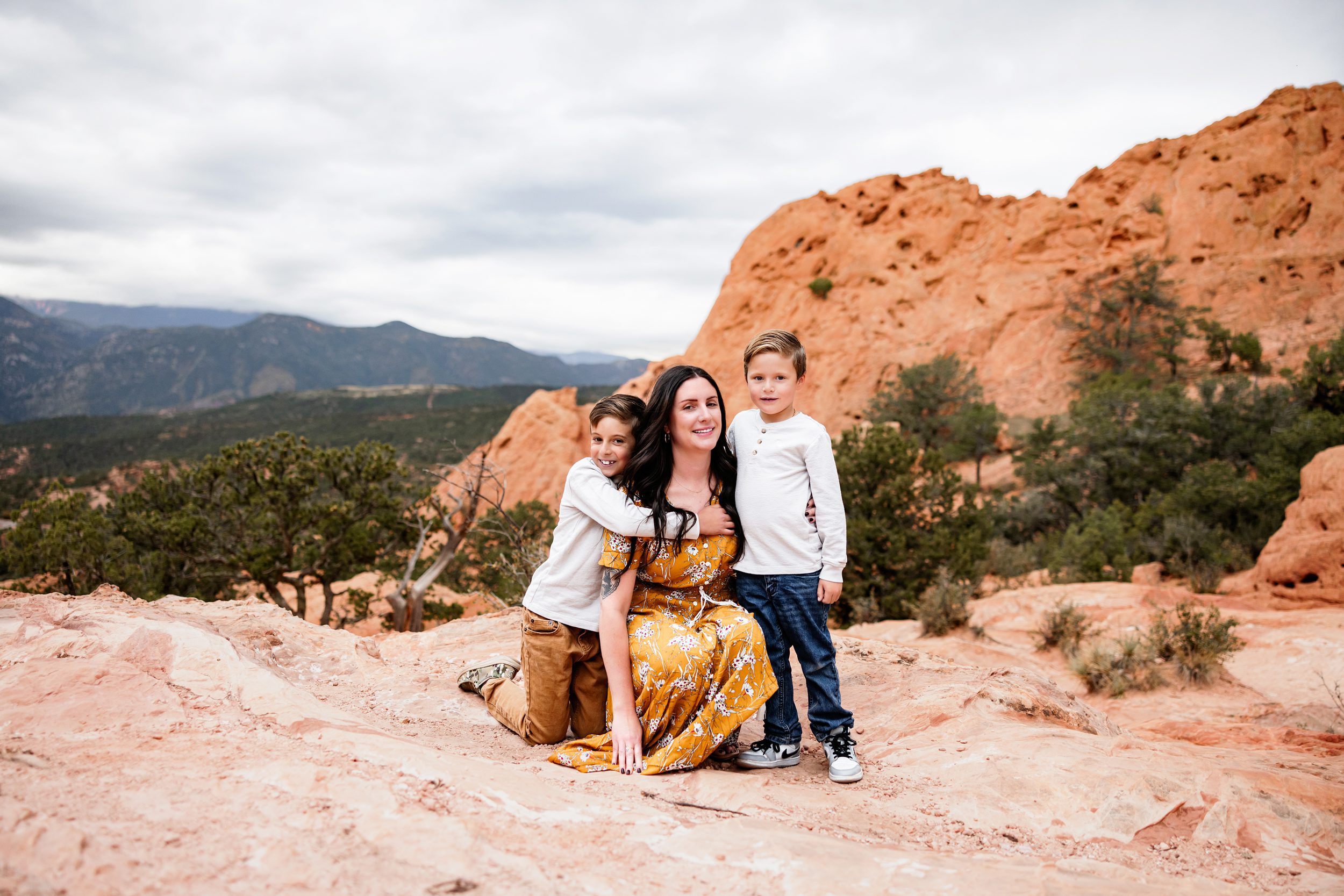 Mom sitting with her two sons on red rocks with mountain views and soft diffused lighting