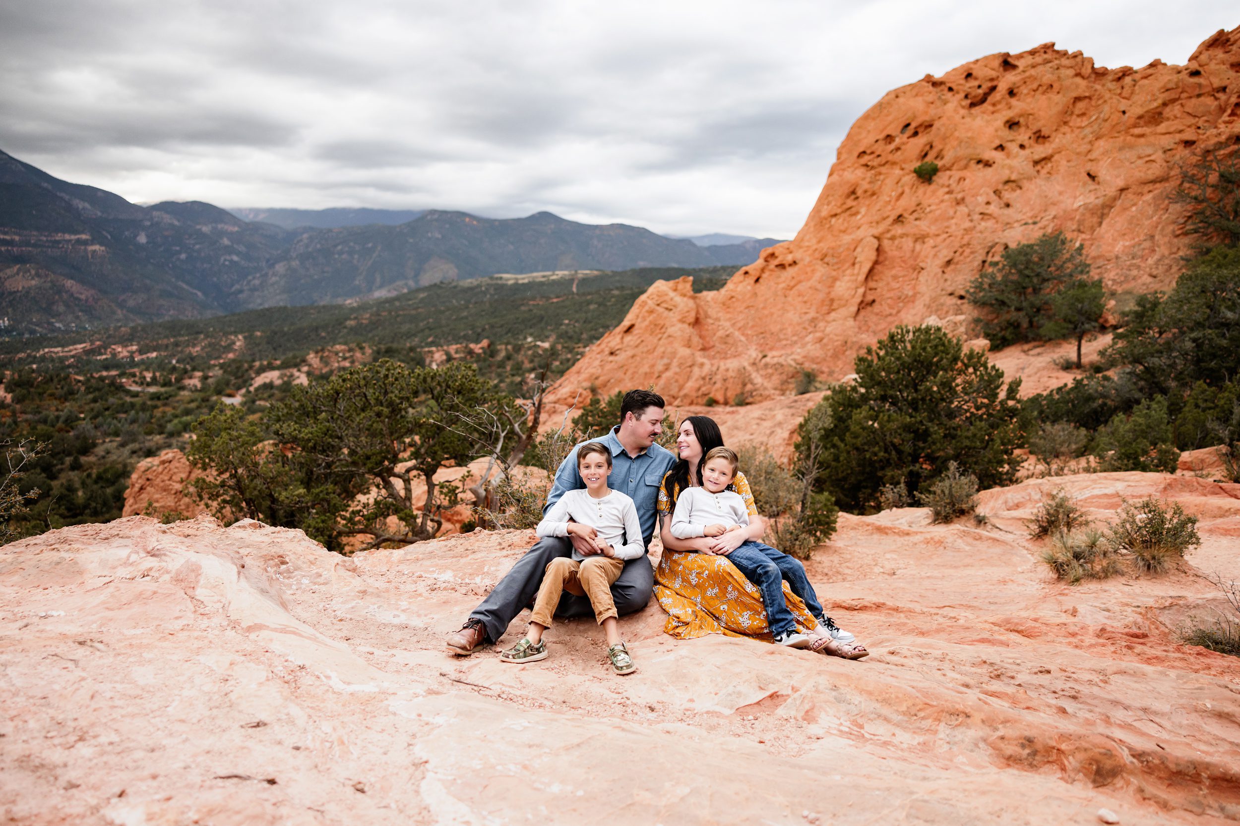 Parents and kids sitting close together on the rocks with cloudy skies and warm tones in the landscape

