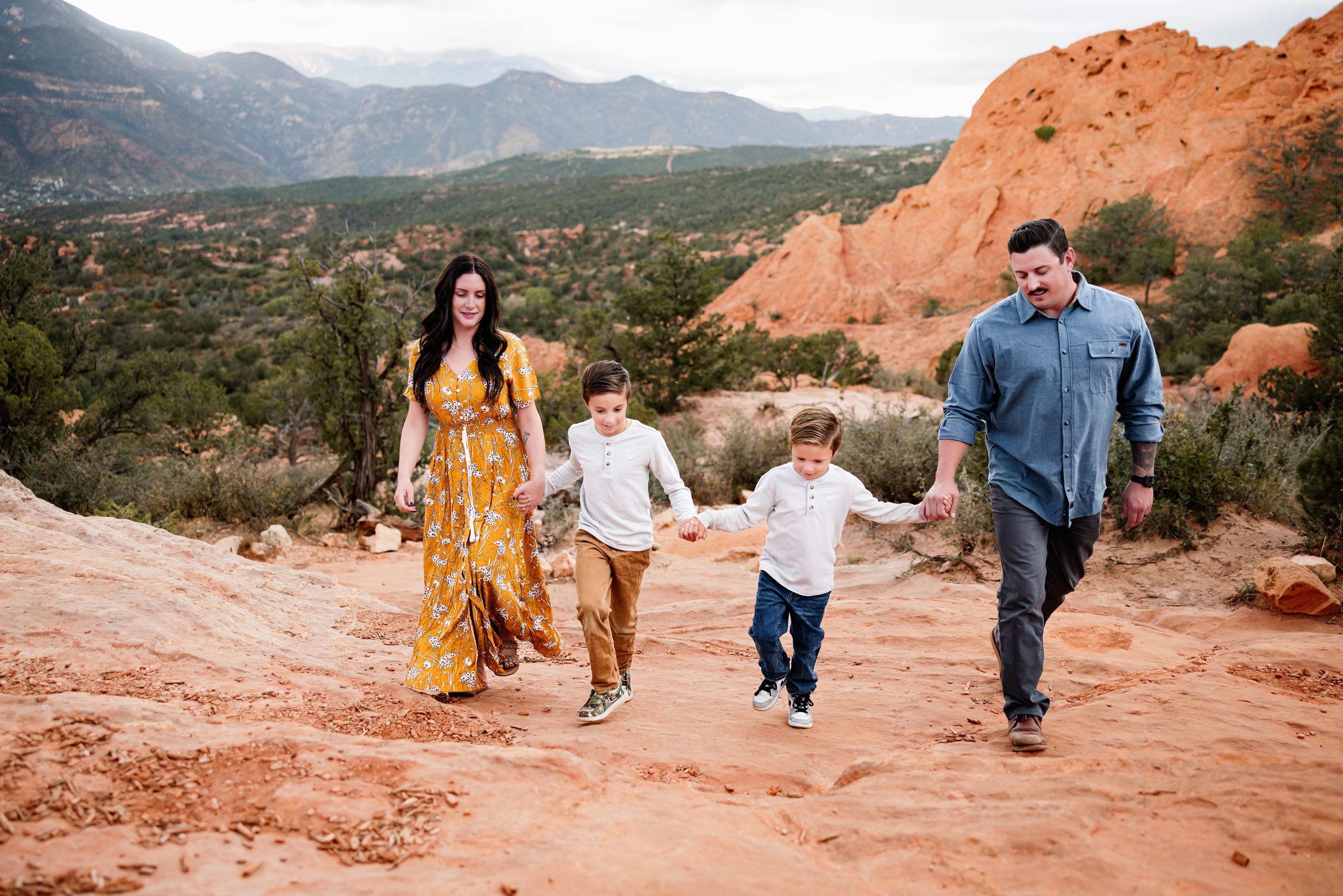 Parents holding hands with their kids while walking through the red rocks with mountains in the background