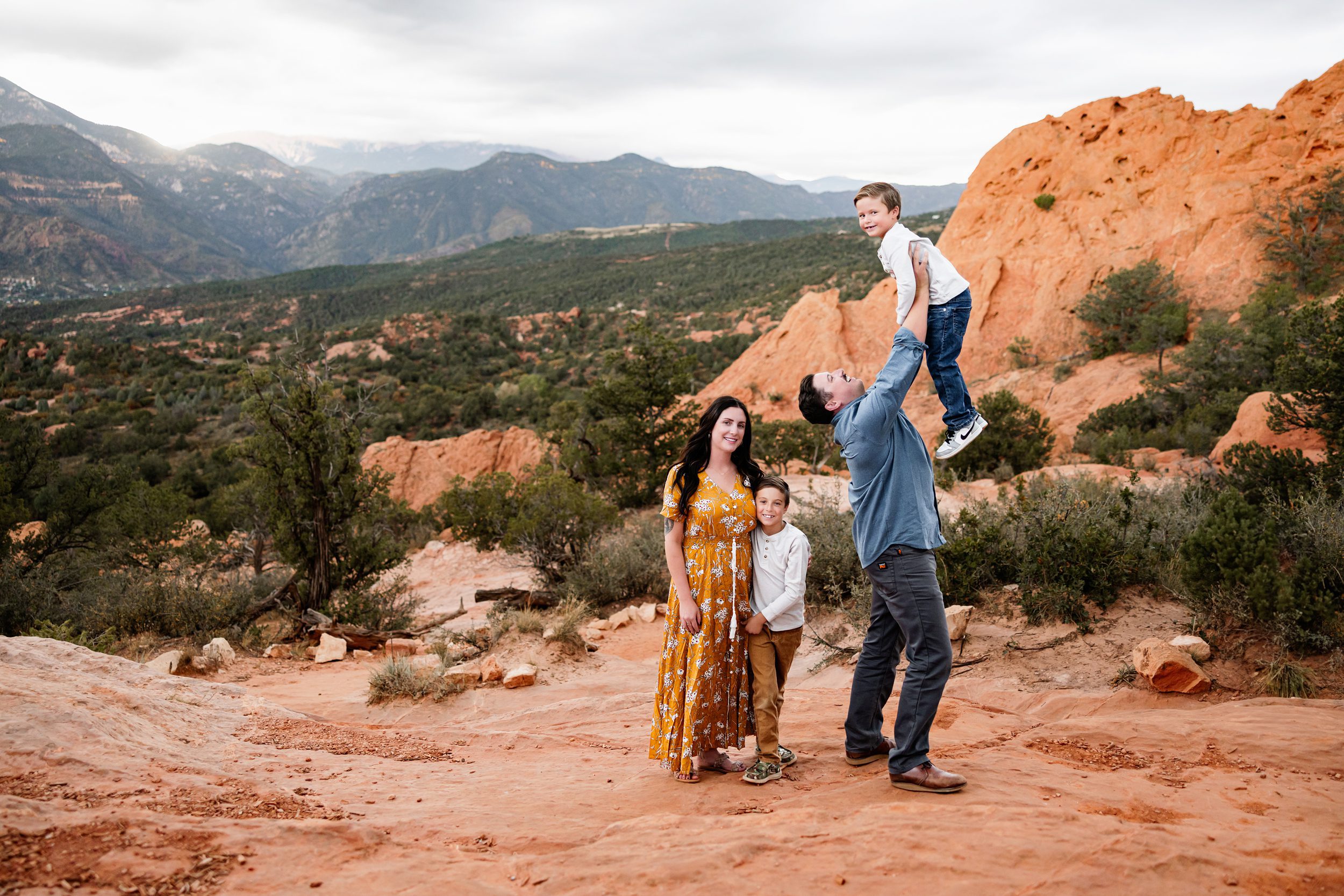 Dad lifting his son into the air while mom and brother smile nearby on a cloudy day in the red rocks