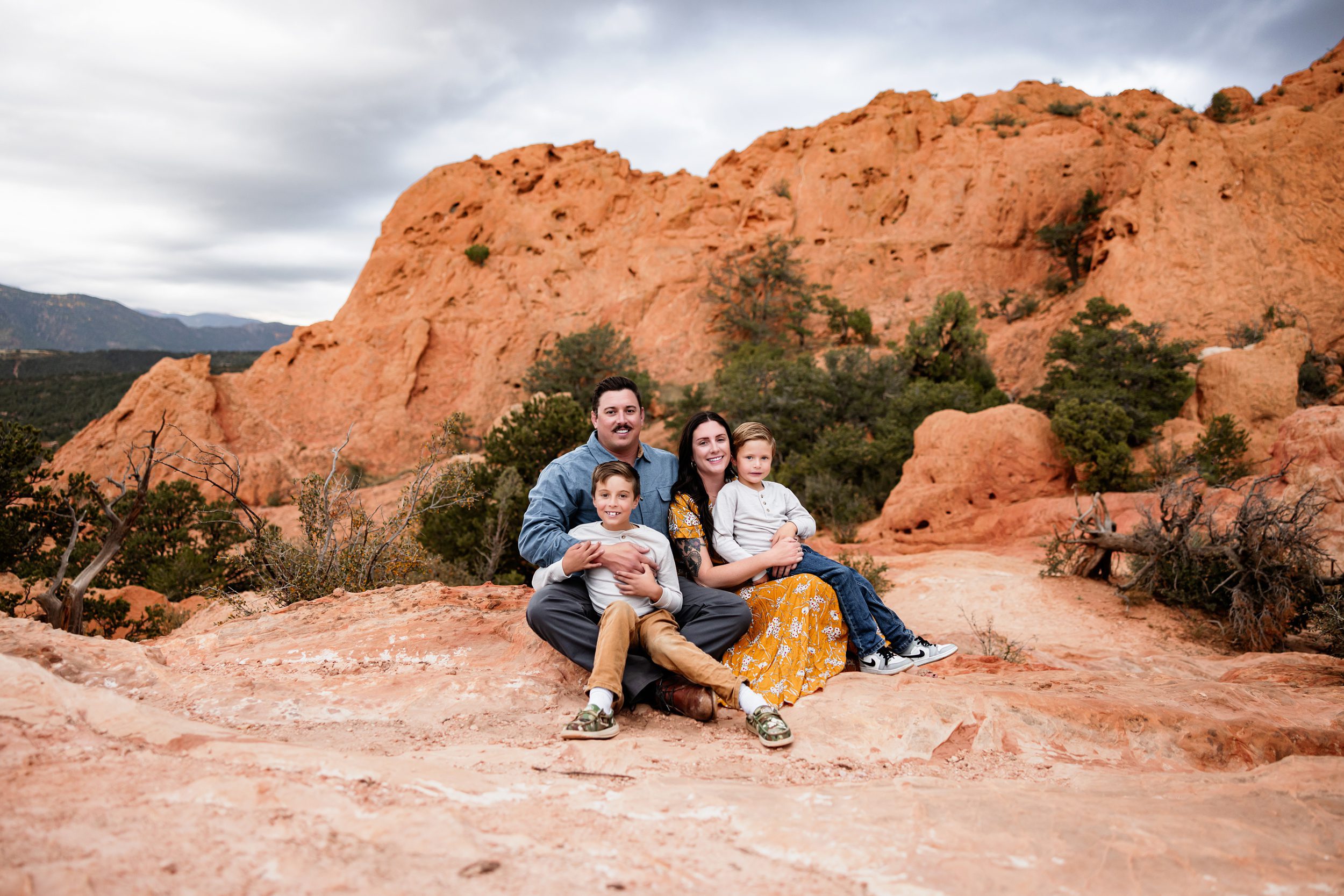 Family sitting together on sandstone rocks with a scenic Colorado backdrop, capturing weather changes on your session day